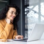 Happy and smiling hispanic businesswoman typing on laptop, office worker with curly hair and