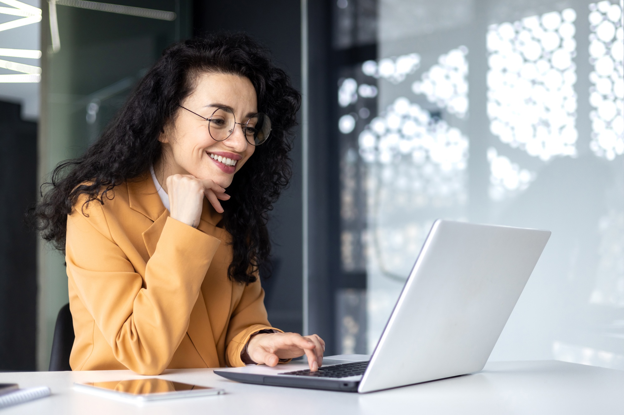Happy and smiling hispanic businesswoman typing on laptop, office worker with curly hair and